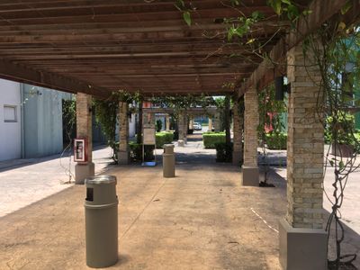 Smoking shed supported by brick columns covered with vines, with cigarette and trash receptacles at the center.